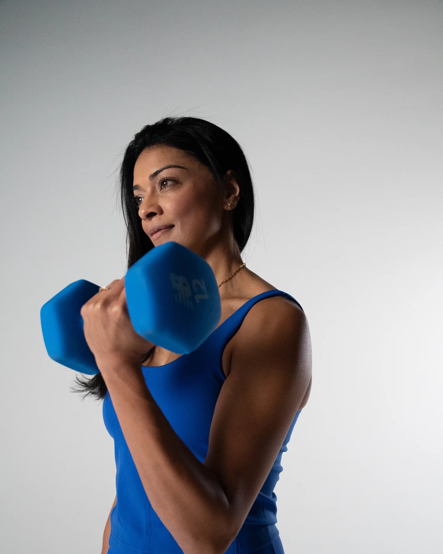 Divya holding a dumbbell at her shoulder, looking off to the side