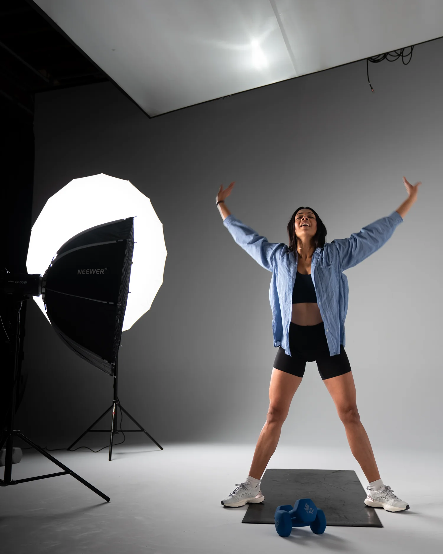 Divya in the studio between takes, arms raised, with the lights and softbox around her