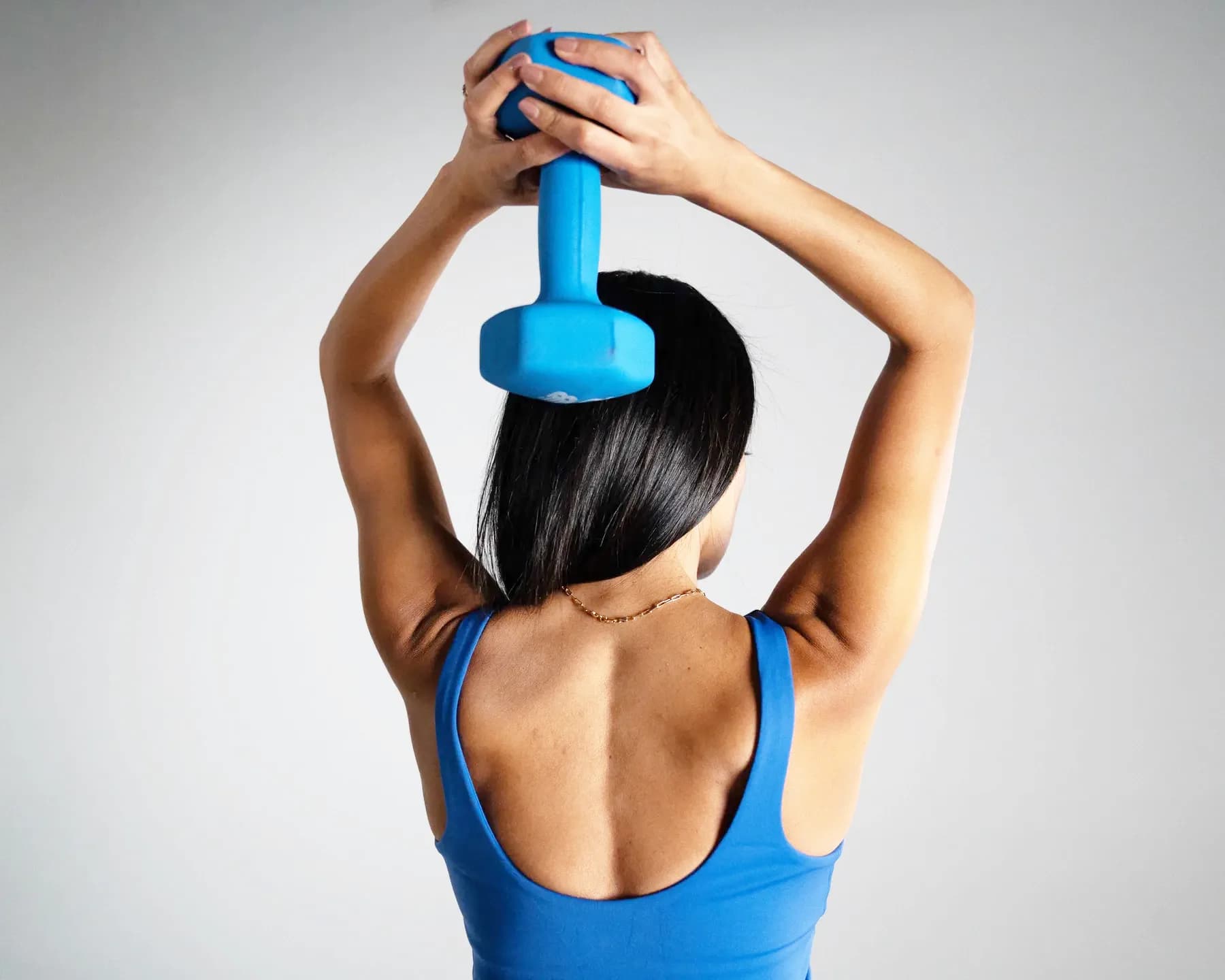 Divya from behind, pressing a dumbbell overhead